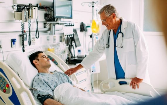 Male doctor talking to a male patient lying in a hospital bed