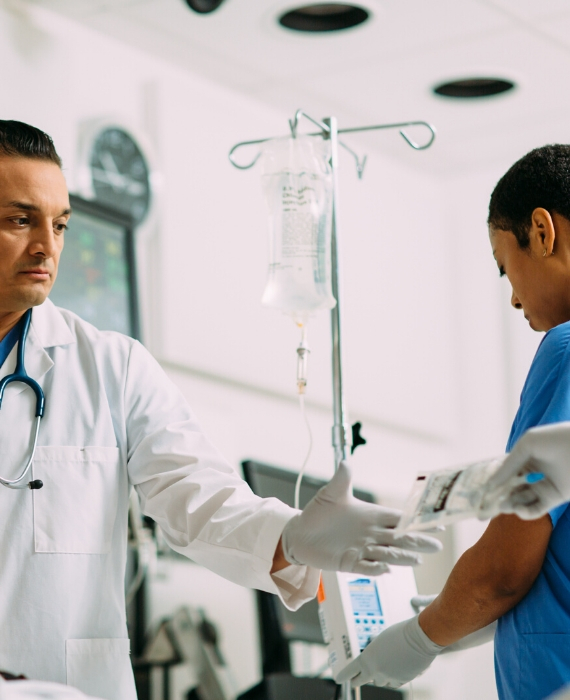 A nurse hands a doctor an IV bag of Baxter Nexterone in a hospital room