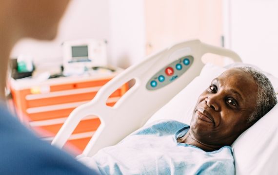 A patient lies in a hospital bed looking at a nurse