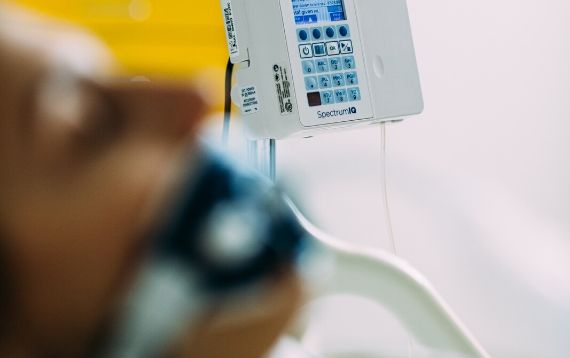 A patient lies in a hospital bed with a Spectrum IQ Infusion Pump near the bed