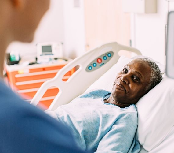 A patient lays in a hospital bed looking at a nurse.