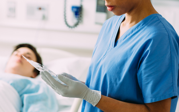 A nurse holds a bag of Baxter product at a patient bedside.