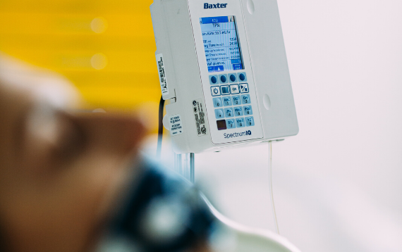 A female patient lies in bed with a Baxter Spectrum IQ infusion system next to the bed
