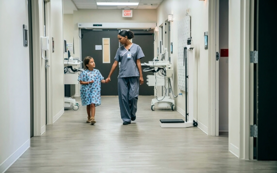 A nurse and pediatric patient walk down a hospital hallway together