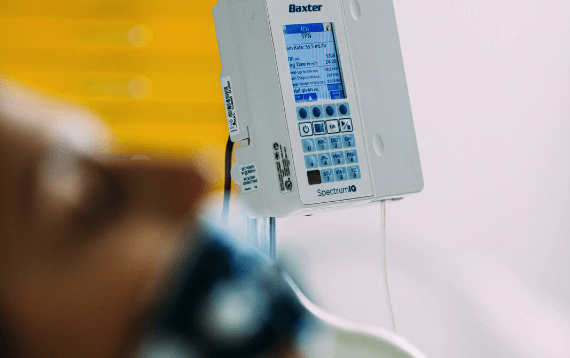 A female patient lies in bed with a Baxter Spectrum IQ infusion system next to the bed