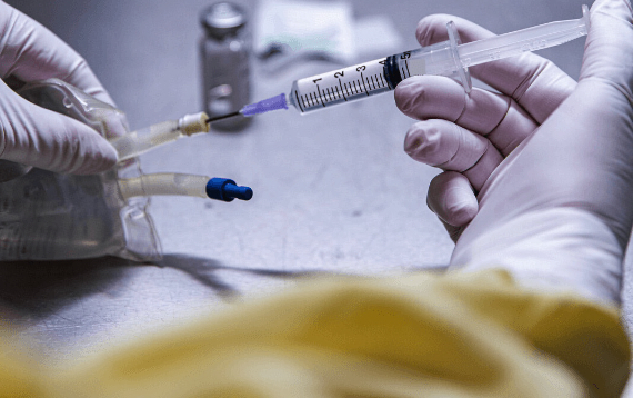 A hospital pharmacist inserts a syringe into an IV bag