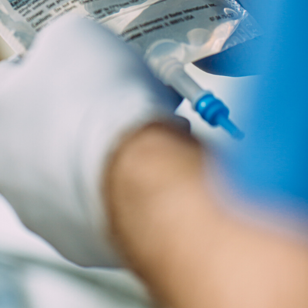 A healthcare provider with a gloved hand holds a bag of Baxter product