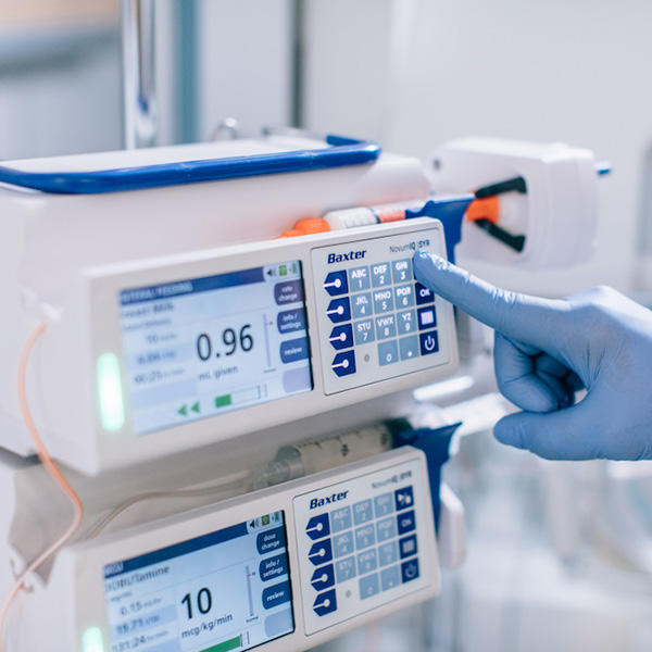 a gloved hand interacts with the Novum IQ Syringe Pump