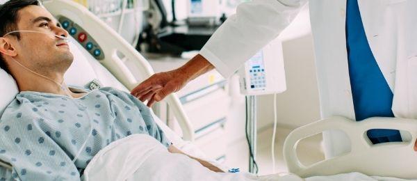 A Spectrum IQ Infusion System sits next to a patient bedside in a hospital while a male patient lays in bed